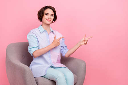 Photo portrait young woman sitting in armchair showing fingers blank space isolated pastel pink color backgroundの写真素材
