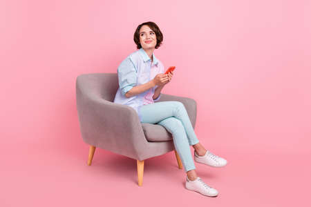 Full length body size photo woman sitting browsing internet on smartphone looking copyspace isolated pastel pink color backgroundの写真素材