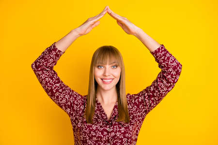 Photo of young cheerful woman happy positive smile show hands roof sign home buy new real estate isolated over yellow color backgroundの写真素材