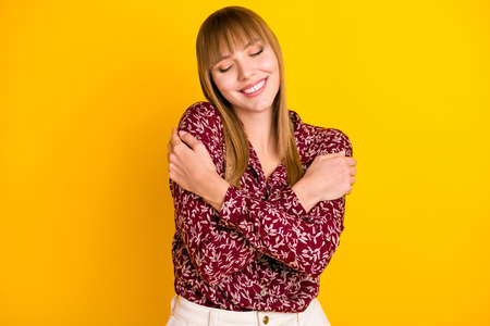 Photo portrait of blonde woman dreaming embracing herself in printed blouse isolated bright yellow color backgroundの写真素材