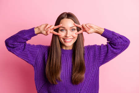 Photo of cheerful young girl show two v-signs cover eye wear violet sweater isolated pink color backgroundの写真素材