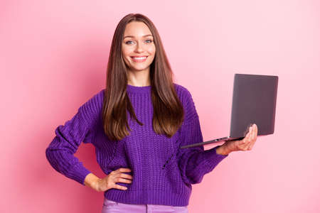 Portrait of positive person put hand on waist hold computer toothy smile wear pullover isolated on pink color backgroundの写真素材