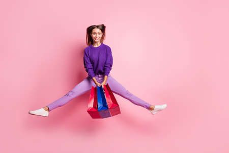 Full body portrait of active cheerful person hold bags jumping legs to sides have fun isolated on pink color backgroundの写真素材