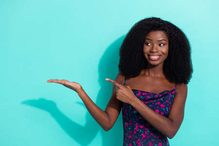 Photo portrait of curious girl smiling looking showing finger holding copyspace isolated on vibrant teal color backgroundの写真素材