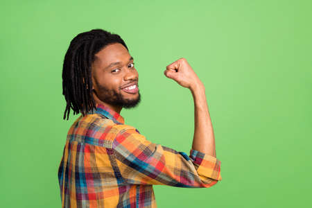 Photo of funny strong dark skin man wear plaid shirt smiling rising fist isolated green color backgroundの写真素材