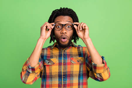 Photo of shocked excited dark skin man wear plaid shirt arms spectacles open mouth isolated green color backgroundの写真素材
