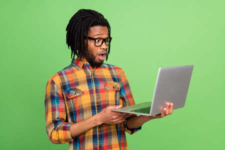 Photo of impressed funky dark skin man wear plaid shirt spectacles looking modern device isolated green color backgroundの写真素材