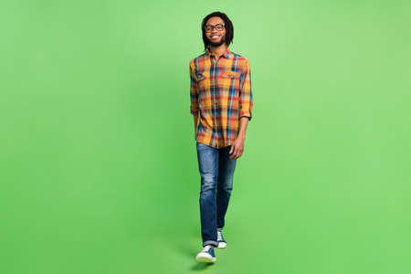 Photo of funky charming dark skin man wear plaid shirt spectacles smiling walking isolated green color backgroundの写真素材