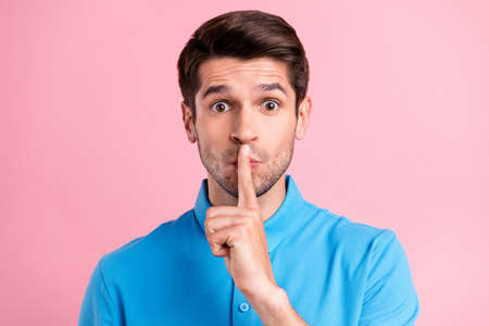 Photo of young serious brown haired male showing silence gesture shut up isolated on pink color backgroundの写真素材