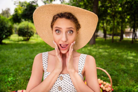 Photo of young amazed shocked astonished woman hold hands face wear hat outdoors outside park streetの写真素材