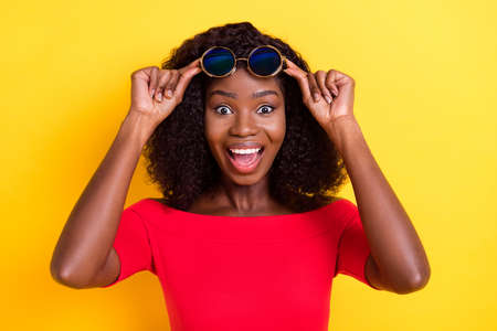 Photo of young happy excited amazed crazy afro girl see huge sale discount wear sunglasses isolated on yellow color backgroundの写真素材