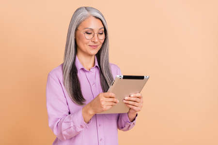 Photo of cute grey hairdo old lady type tablet wear spectacles violet shirt isolated on beige color backgroundの写真素材