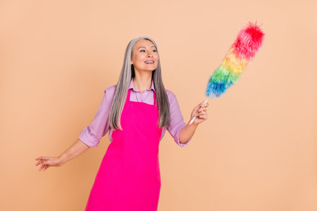 Portrait of attractive dreamy cheery gray-haired woman wiping dust home isolated over beige pastel color backgroundの写真素材