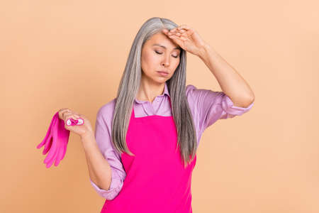 Portrait of attractive tired sad gray-haired woman doing clean up isolated over beige pastel color backgroundの写真素材
