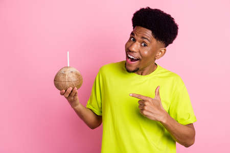 Portrait of attractive trendy cheerful guy demonstrating coconut juice party holiday isolated over pink pastel color backgroundの写真素材
