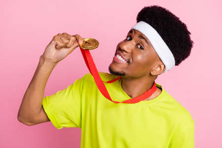Photo of cheerful young dark skin positive man hold hand golden medal winner isolated on pink color...
