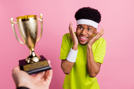 Portrait of attractive cheerful amazed guy sportsman receiving prize isolated over pink pastel color backgroundの写真素材
