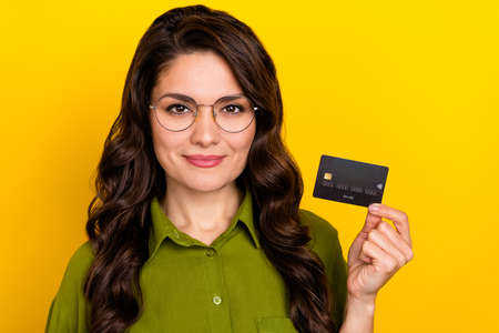 Photo of cheerful banker lady demonstrate debit card wear glasses green shirt isolated yellow color backgroundの写真素材