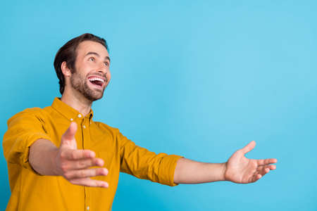 Profile photo of positive hopeful guy look empty space catch hands wear yellow shirt isolated blue...