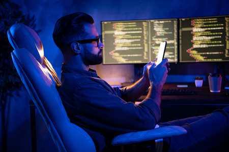 Profile portrait of young serious guy write typing email telephone sitting chair dark loft space insideの写真素材