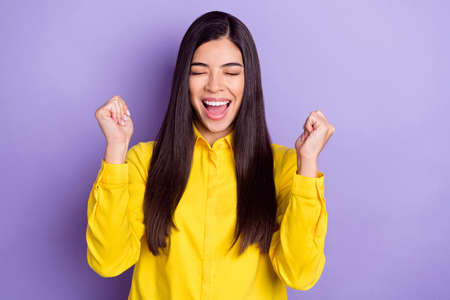 Photo of brown hairdo celebrate young lady hands fists closed eyes yell wear yellow shirt isolated on purple backgroundの写真素材