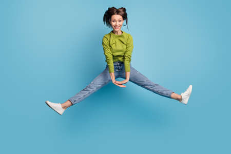 Photo of positive childish cute lady jump hold hands wear green shirt jeans footwear isolated blue color backgroundの写真素材