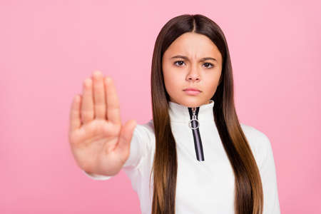 Photo of angry brunette little girl show stop wear white pullover isolated on pastel pink color backgroundの写真素材