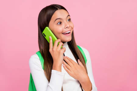 Photo of optimistic brunette small girl talk telephone wear white sweater bag isolated on pink color backgroundの写真素材