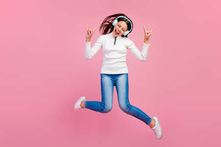 Full size photo of cool brunette teen school girl jump listen music show rock sign wear sweater jeans shoes isolated on pink color backgroundの写真素材