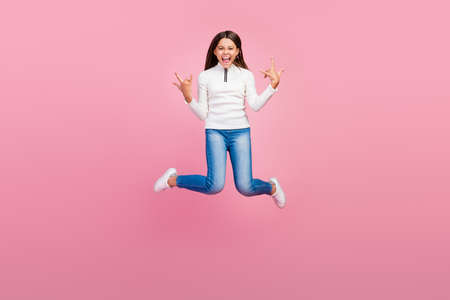 Full body photo of cool brunette small girl jump show rock sign wear sweater jeans footwear isolated on pink color backgroundの写真素材