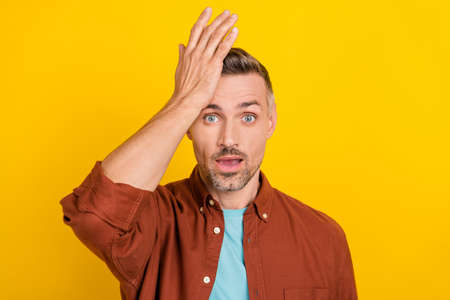 Photo of impressed mature grey hairdo man palm face wear clothes isolated on yellow color backgroundの写真素材