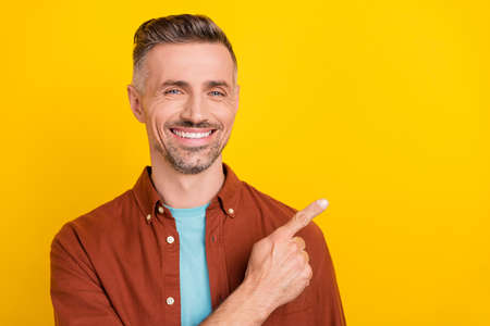 Photo of optimistic mature grey hairdo man index empty space wear brown shirt isolated on yellow color backgroundの写真素材
