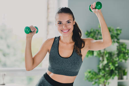 Photo of pretty charming lady wear sport outfit smiling holding dumbbells indoors home houseの写真素材