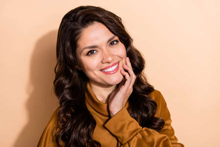 Portrait of attractive sweet cheerful wavy-haired woman touching face good mood isolated over beige...