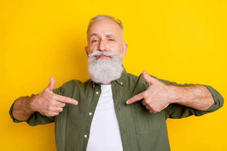 Photo portrait of senior man in green shirt pointing fingers at himself demonstrating confident...