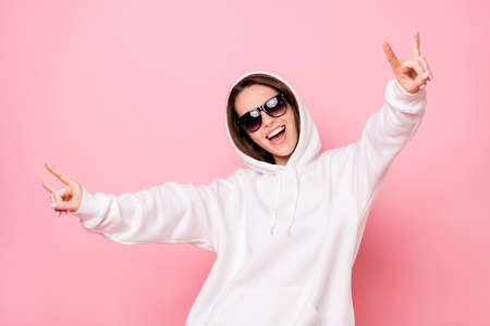Photo of charming funky young lady wear white hoodie smiling showing hard rock sign isolated pink color backgroundの写真素材