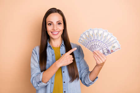 Portrait of gorgeous positive girl point fingers money recommending advertise isolated on beige...