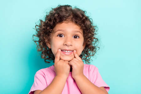 Photo of young small latin girl happy positive smile fingers touch mouth toothy isolated over turquoise color backgroundの写真素材