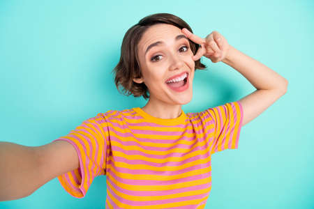 Photo of excited funny young woman dressed striped t-shirt tacking selfie v-sign cover eye isolated...