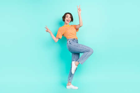 Photo of charming cute young woman dressed striped t-shirt smiling dancing showing v-signs isolated teal color backgroundの写真素材