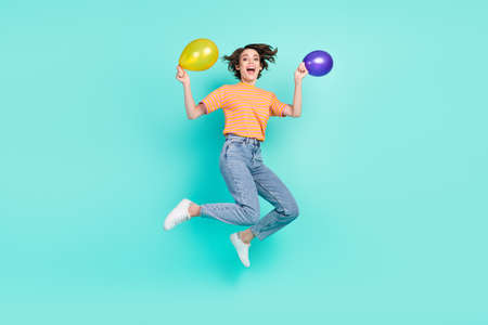 Photo of sweet excited young woman dressed striped t-shirt smiling jumping holding balloons isolated teal color backgroundの写真素材
