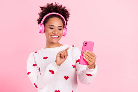 Photo of youth pretty african girl look smartphone choose song headphones isolated over pink color...