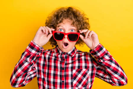 Photo of hooray orange curly hairdo little boy wear eyewear red checkered shirt isolated on yellow color backgroundの写真素材