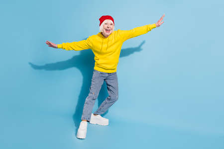 Full body photo of cheerful positive funky old woman hands plane wings smile isolated on blue color backgroundの写真素材