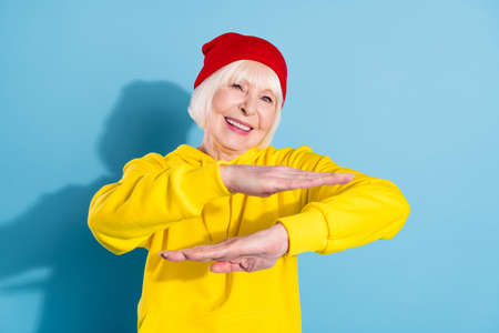 Photo of attractive old cool woman dance hip-hop wear red hat hoodie isolated on blue color backgroundの写真素材