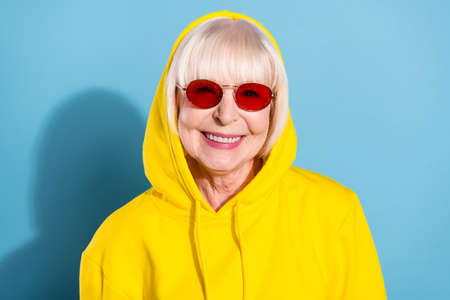 Photo of charming old cheerful woman wear cool sunglass good mood hood isolated on blue color backgroundの写真素材