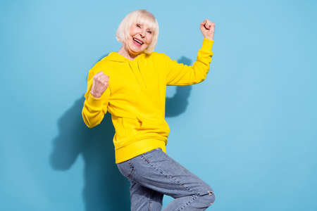 Photo of cheerful sweet nice old woman raise fists wear casual clothes winner isolated on blue color backgroundの写真素材