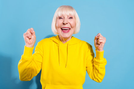 Photo of cheerful nice old positive lady raise fists winner good mood isolated on pastel blue color...