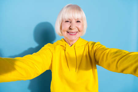 Photo of cheerful positive charming old woman make selfie camera smile isolated on blue color backgroundの写真素材