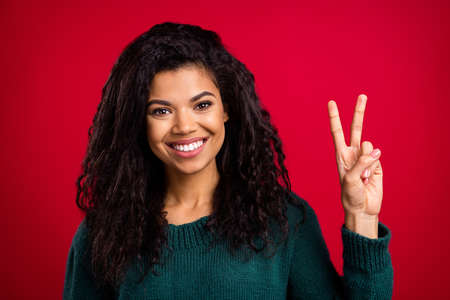 Photo of pretty charming dark skin lady wear green sweater showing v-sign smiling isolated red color backgroundの写真素材
